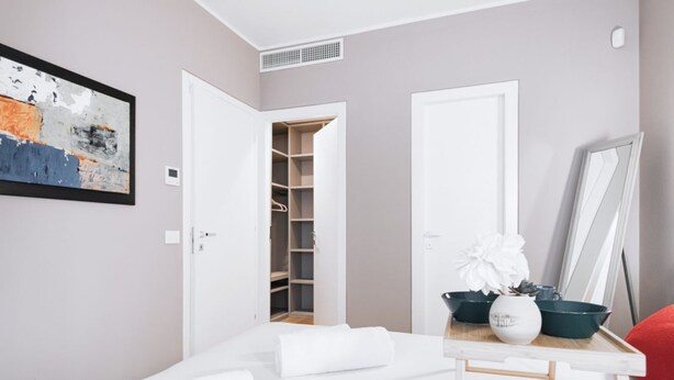 A modern bedroom with a neatly made bed, a bedside table with a vase and a bowl, and a closet with open doors. - Easylife - Elegant flat at Castello Sforzesco (Milan)