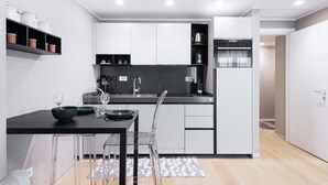 A modern kitchen with white cabinets, a black countertop, and a dining area with a black table and clear chairs. - Easylife - Elegant flat at Castello Sforzesco (Milan)