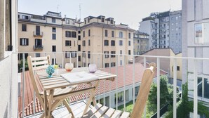Ein Balkon mit Holztisch und -stühlen, mit Blick auf eine Reihe von Wohnhäusern.