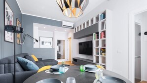 Ein modernes Wohnzimmer mit einem runden Esstisch, einem grauen Sofa und einem an der Wand befestigten Fernseher.