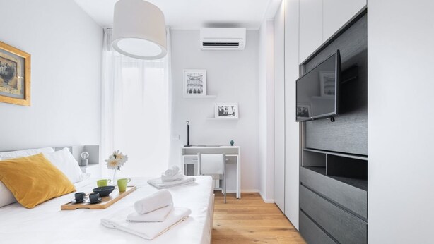 Ein modernes Schlafzimmer mit Bett, Nachttisch und einem an der Wand montierten Fernseher.