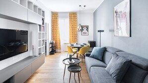 Ein modernes Wohnzimmer mit einem grauen Sofa, einem Esstisch mit gelben Stühlen und einem Fernseher auf einem weißen Schrank.