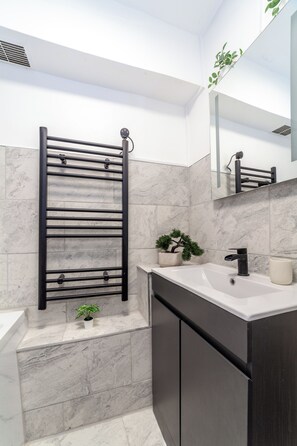 A modern bathroom with a black towel rack, a white sink, a potted plant, and a large mirror.