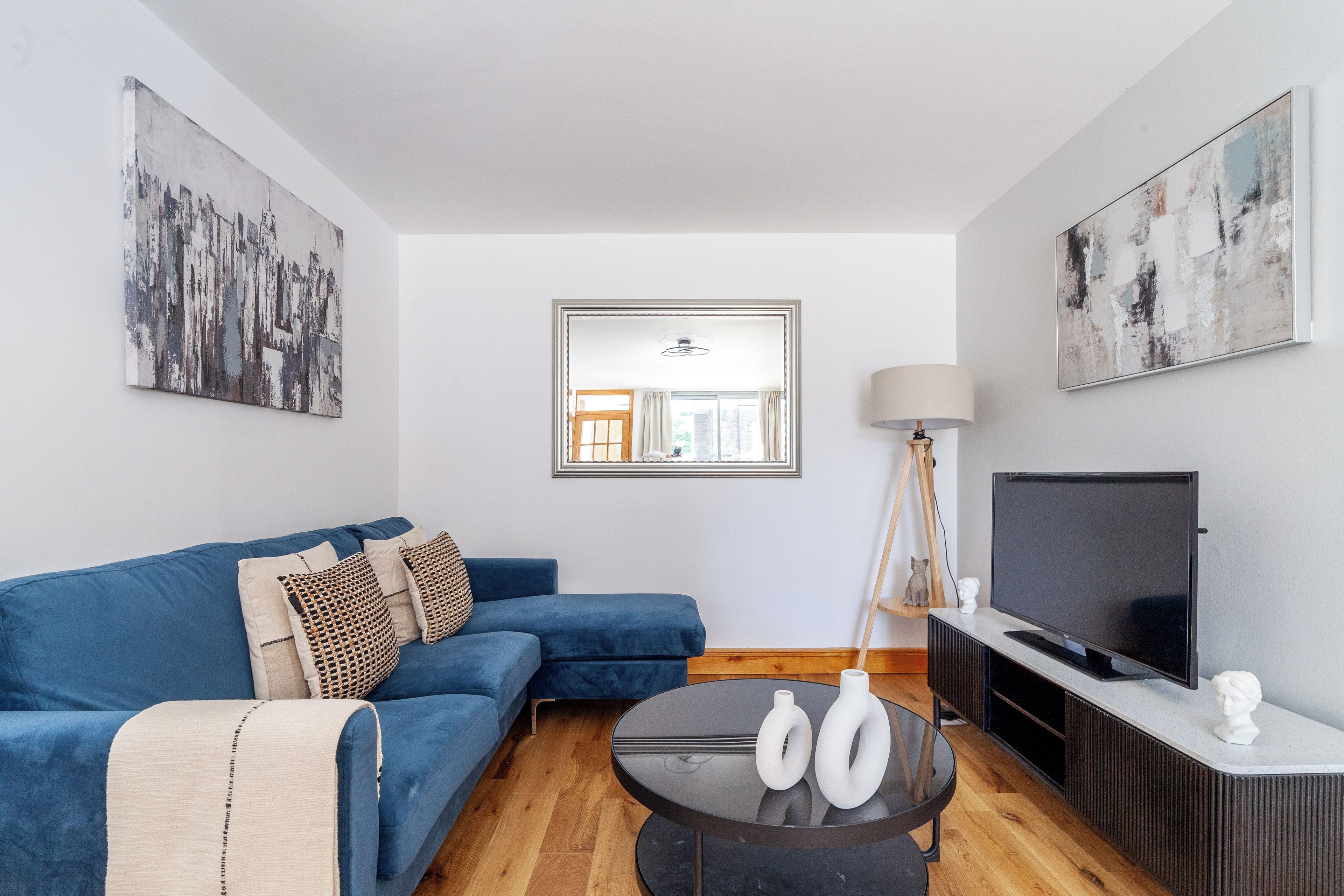Een moderne woonkamer met een blauwe bank, een salontafel, een televisie en kunstwerken aan de wanden.