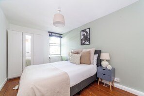 A bedroom with a bed, bedside table, lamp, and artwork on the wall.
