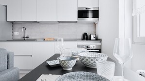 Una cocina moderna con armarios blancos, electrodomésticos de acero inoxidable y una zona de comedor con vajilla estampada.