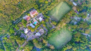 An aerial view of a residential area with multiple buildings, a large green field, and a swimming pool. - Rajpracha Pakchong (Pak Chong)