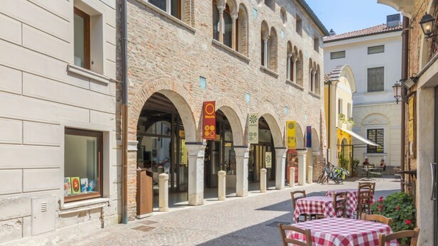 A cobblestone street with outdoor seating, stone buildings, and arches. - AureliaHome@Pescheria (Treviso)