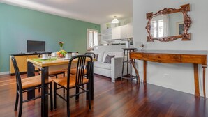A dining area with a wooden table and chairs, a kitchen in the background, and a large mirror on the wall. - AureliaHome@Pescheria (Treviso)