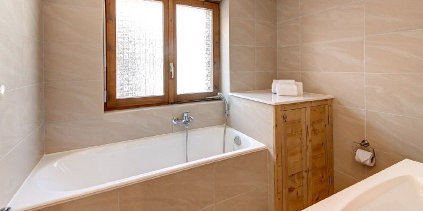 A bathroom with a bathtub, wooden cabinet, and a window.