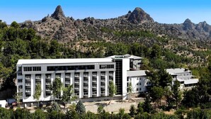 A modern building with multiple floors, surrounded by trees and mountains in the background. - Celik Hanim Termal Otel & Spa (Ulukisla)