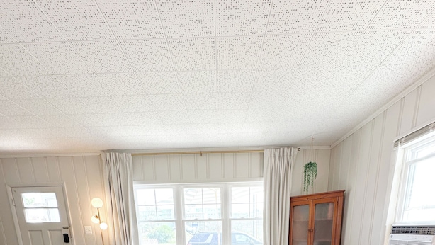 Ein Wohnzimmer mit einem Ecksofa, zwei runden Hocker und einem großen Fenster mit Vorhängen.