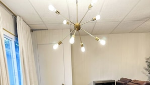 Ein Essbereich mit einem Holztisch, weißen Stühlen, einer modernen Pendelleuchte und einem Fernseher.