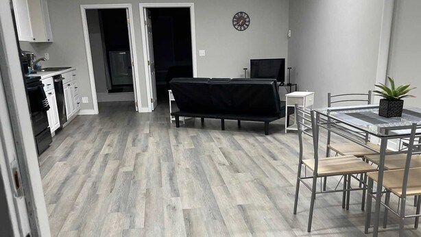 A modern kitchen with white cabinets, a black countertop, and a dining area with a table and chairs. - Private Apartment in Southbury 102 (Southbury)
