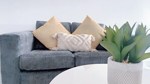 A grey sofa with three cushions, a white textured pillow, and a potted plant on a white table. - HushHavenHull-SLEEP 4| Wifi+Netflix| SnookerTable (Kingston upon Hull)