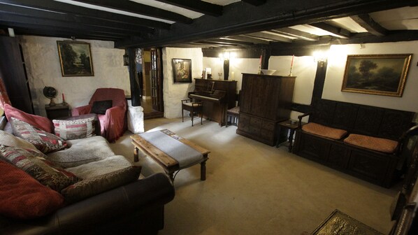 A traditional room with a wooden bench, a piano, a red armchair, and a sofa with patterned cushions. - Cozy Room with En-suite in 16th century Cottage (Coventry)