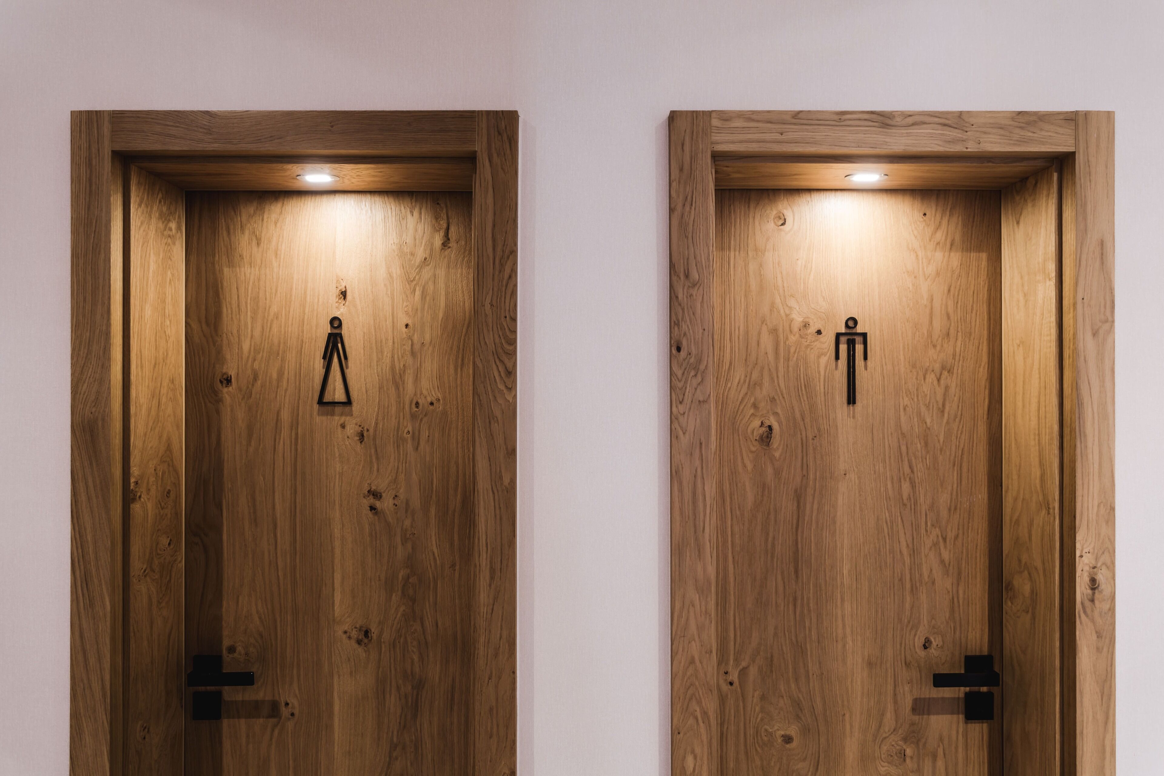 Two wooden doors with a light fixture above each, one with a triangular symbol and the other with a human figure symbol.