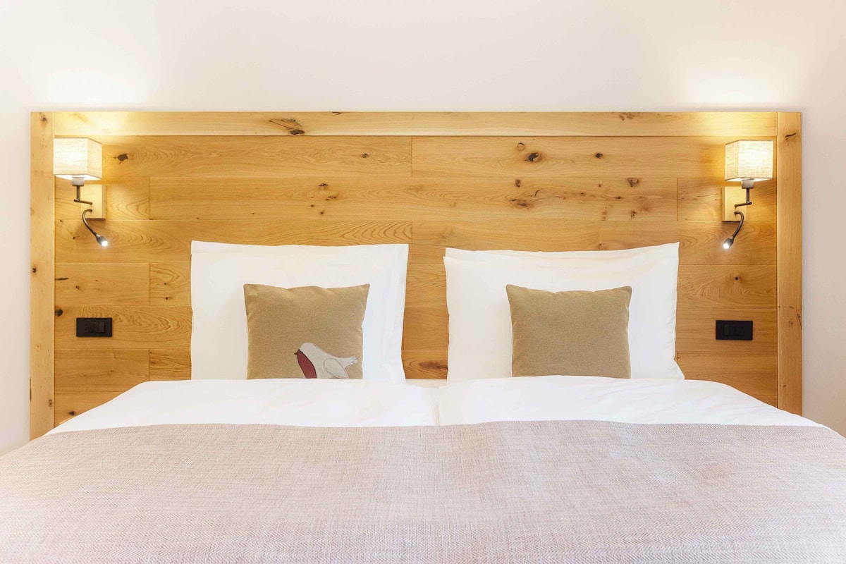 A double bed with a wooden headboard, two wall-mounted lamps, and two pillows with a bird design.