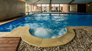 Piscina interior com hidromassagem, deck de madeira e parede de pedra.
