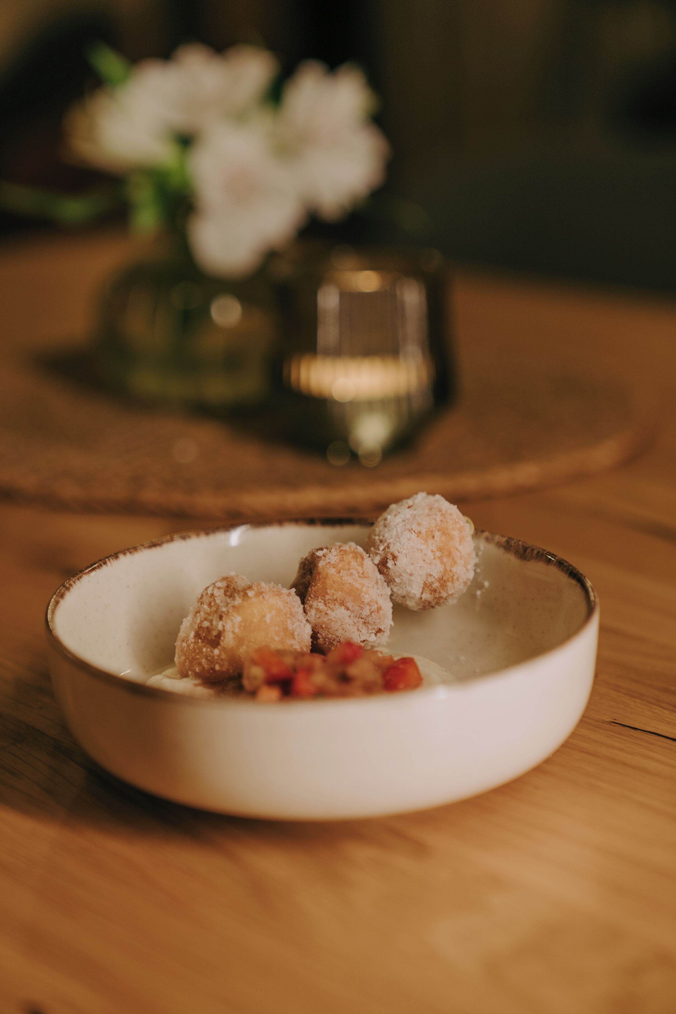 A white bowl with three sugar-coated items on a wooden table.