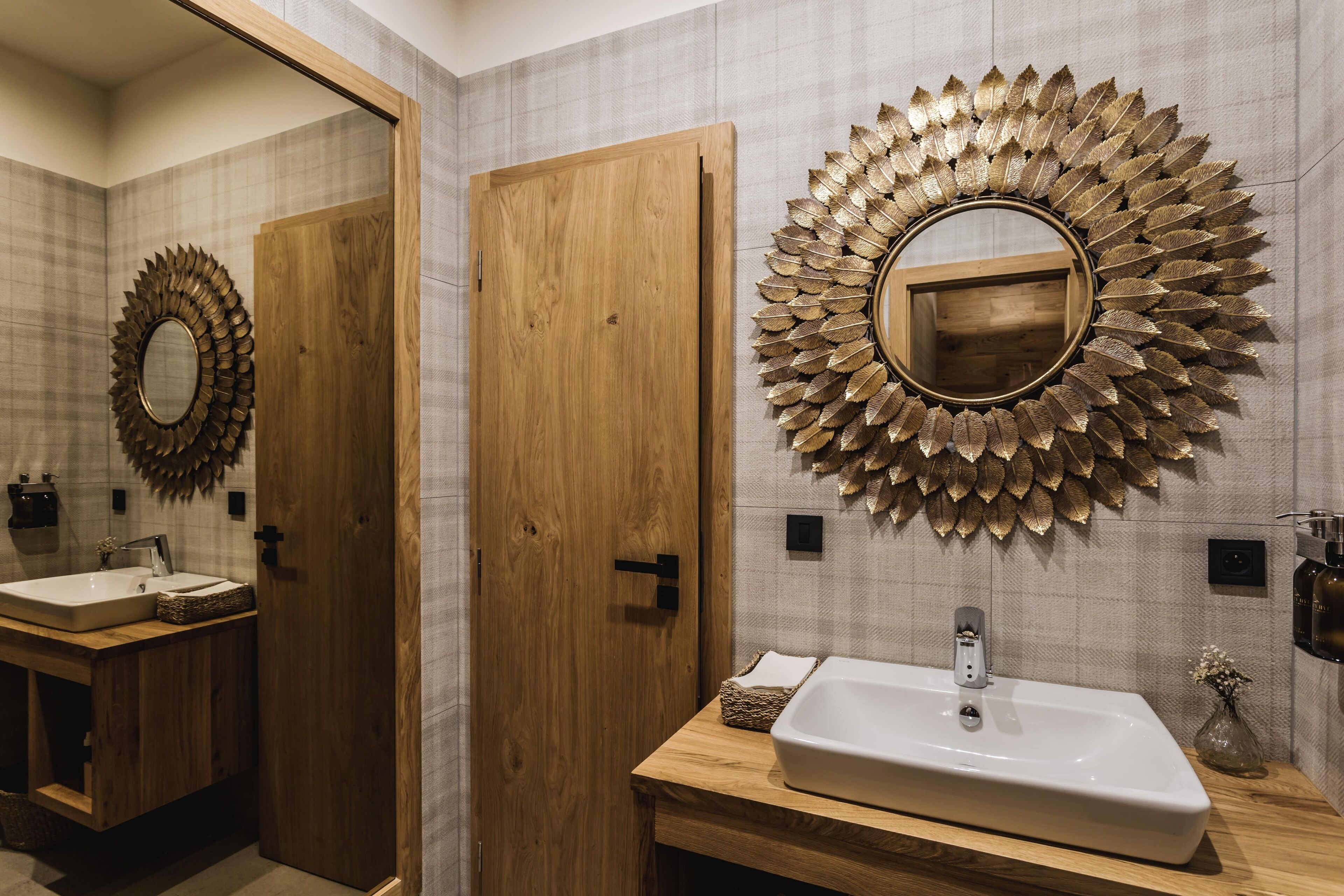 A bathroom with a wooden vanity, a large mirror with a leaf-like frame, and a wall-mounted sink.