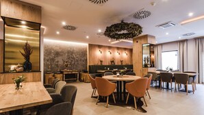 Uma sala de jantar moderna com mesas e cadeiras de madeira, um espelho grande e plantas decorativas.