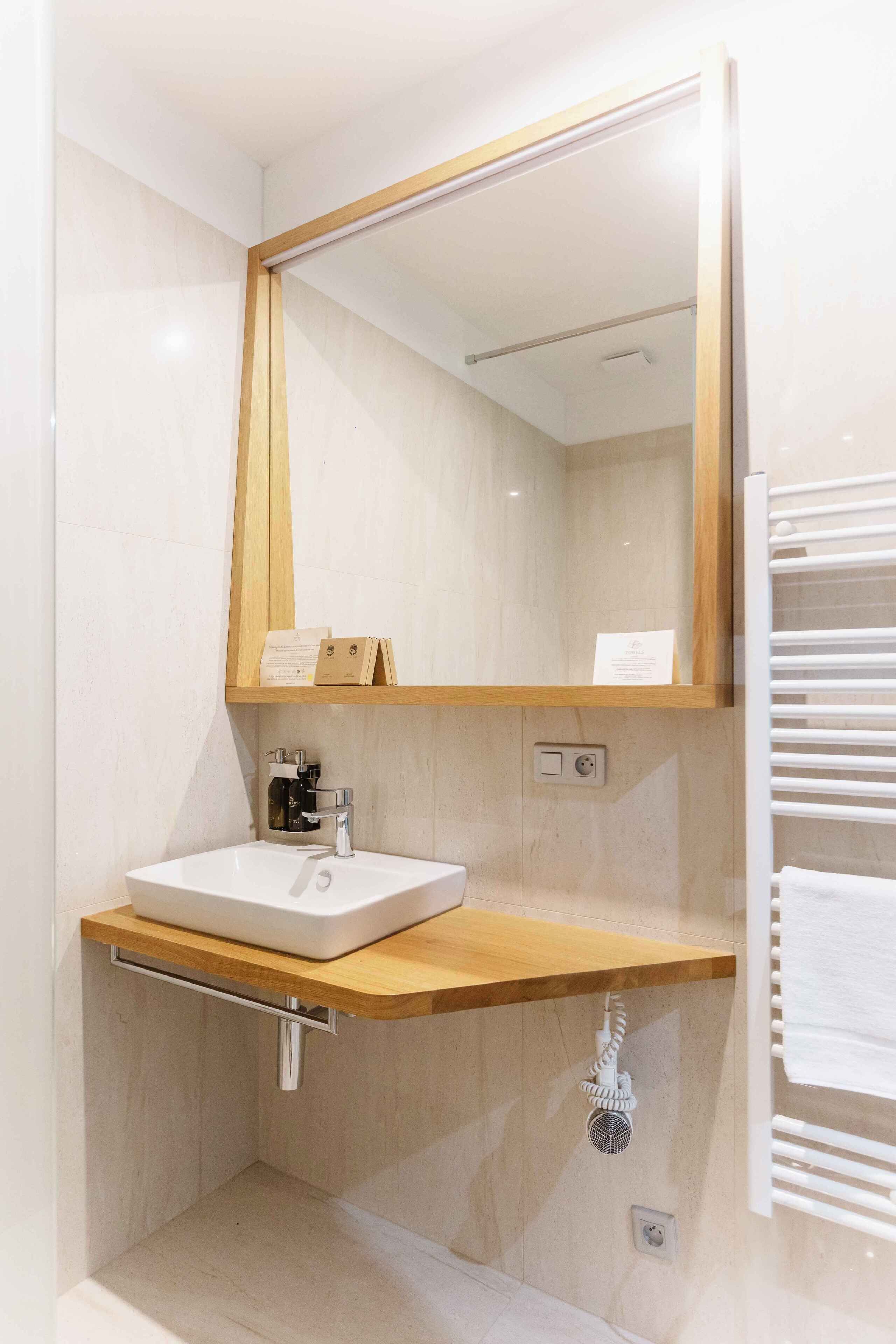 A bathroom with a white sink, a wooden vanity, a mirror, and a towel rack.