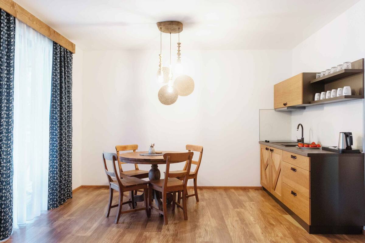 A compact kitchen with a dining table, chairs, wooden cabinets, and a hanging light fixture.