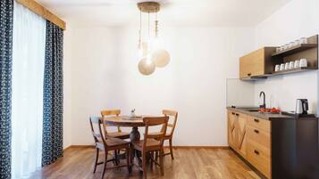 A compact kitchen with a dining table, chairs, wooden cabinets, and a hanging light fixture.