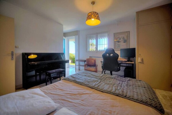 Une chambre d’hôtel avec un lit, un bureau avec un ordinateur, une chaise et un piano.