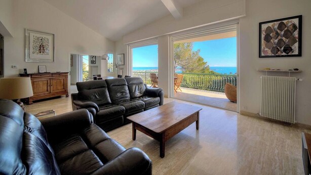 A spacious living room with a large window, a black leather sofa, a wooden coffee table, and a view of the sea. - FRGK Villa Le Petit Bois Panoramic View, Lush Ga (vallauris)