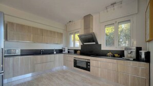 A modern kitchen with built-in appliances, a large window, and a view of greenery outside. - FRGK Villa Le Petit Bois Panoramic View, Lush Ga (vallauris)