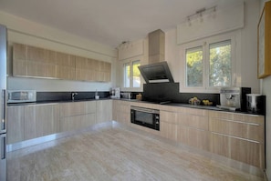 A modern kitchen with built-in appliances, a large window, and a view of greenery outside. - FRGK Villa Le Petit Bois Panoramic View, Lush Ga (vallauris)
