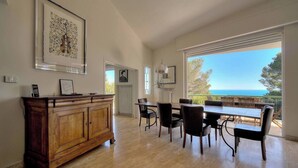 A dining area with a wooden cabinet, framed artwork, and a table with chairs. - FRGK Villa Le Petit Bois Panoramic View, Lush Ga (vallauris)