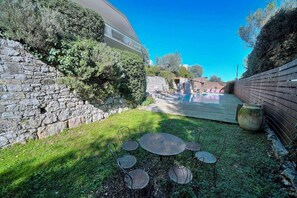 Un mur de pierres, une terrasse en bois et une piscine dans un jardin.