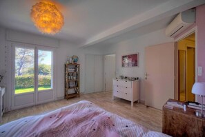 A bedroom with a bed, a dresser, a wardrobe, a globe, and a window with a view of greenery.