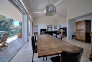 Een ruime eethoek met een lange houten tafel en stoelen, een hanglamp en uitzicht op de omgeving.