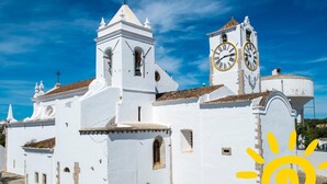 A white church with a bell tower and two clocks, surrounded by cobblestone streets and greenery. - Studio Apartment with Sea View (Cabanas de Tavira)