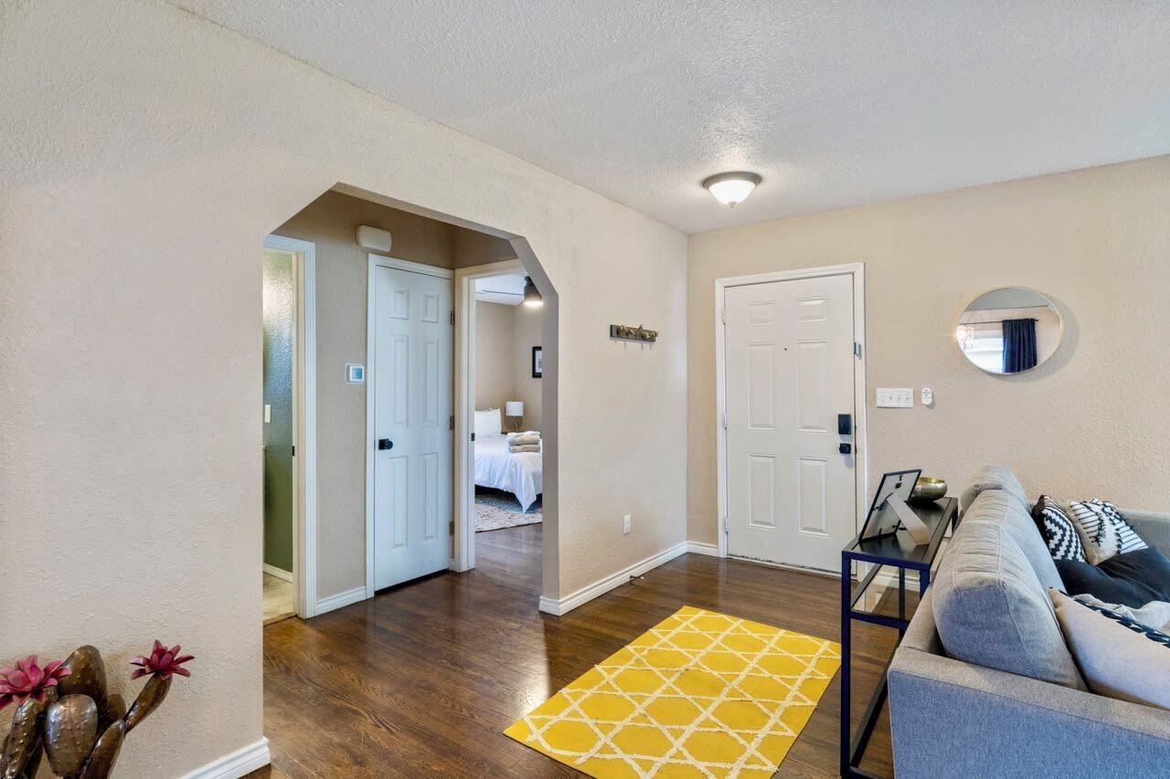 A hallway with a yellow rug, a gray sofa, and a bed in the background.