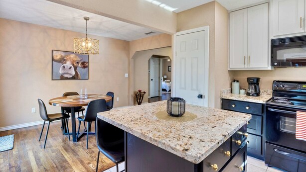 Uma cozinha moderna com bancadas de granito, uma sala de jantar com mesa e cadeiras redondas, e uma porta visível que dá para outro espaço.