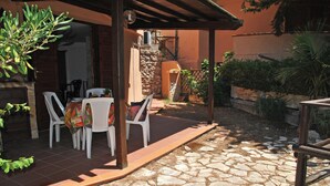 An outdoor patio with stone flooring, white plastic chairs, and a table with a colorful tablecloth. - Marilena Cottage Between sea and Nature (Sperlonga)