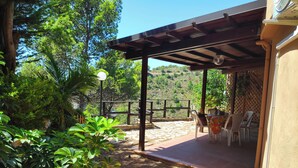 A covered outdoor patio with stone flooring, a wooden pergola, and a view of a hillside. - Marilena Cottage Between sea and Nature (Sperlonga)