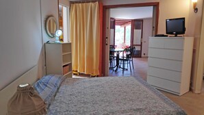 A bedroom with a bed, a desk with a computer, a wardrobe, and a dining area with chairs and a table. - Marilena Cottage Between sea and Nature (Sperlonga)