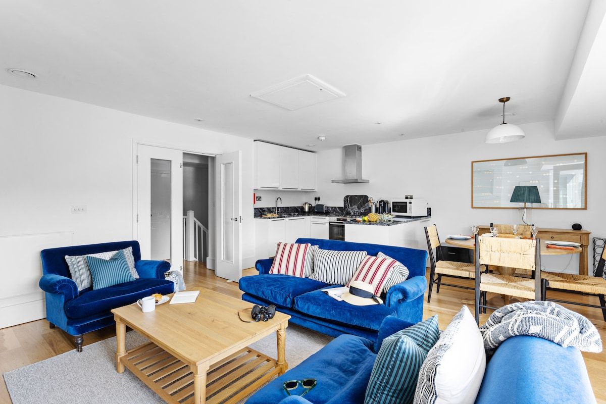 Een moderne woonkamer met een blauwe zithoek, een houten salontafel en een eethoek met een tafel en stoelen.