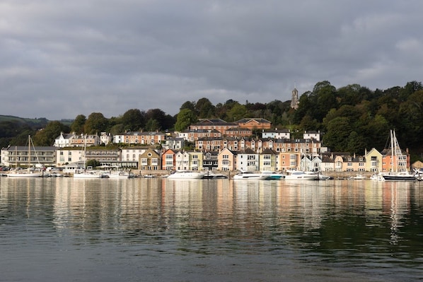 Une propriété située au bord de l’eau, avec une série de bâtiments, une marina remplie de bateaux et, en arrière-plan, une colline parsemée d’arbres.