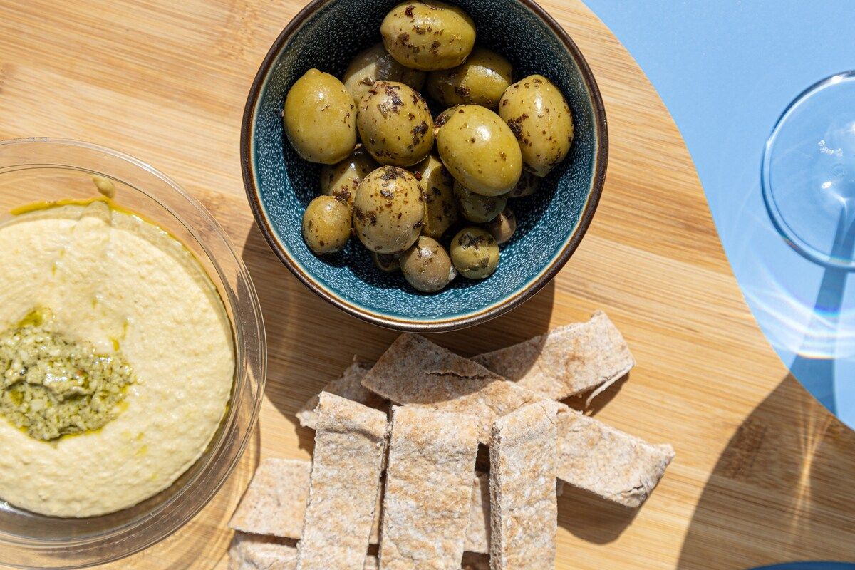 A bowl of olives, a bowl of hummus, and pita chips on a wooden table.