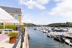 A marina with boats docked, a building with a stone facade, and outdoor seating with a potted plant.