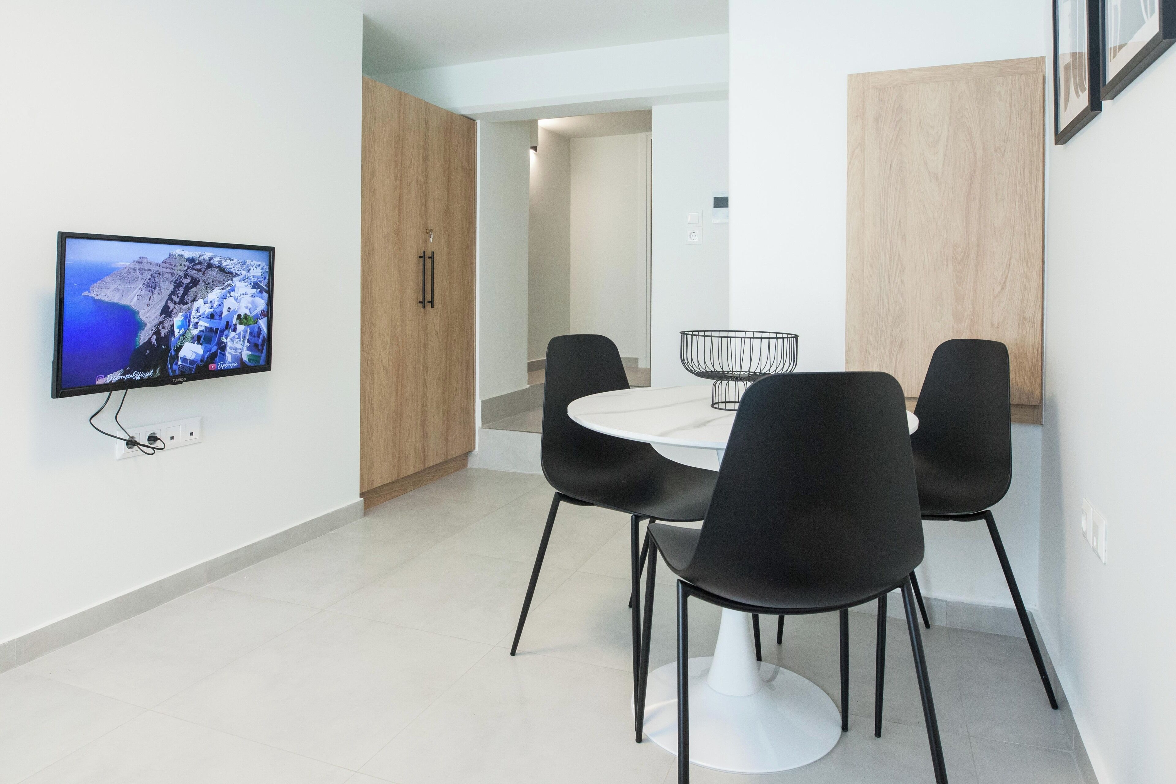 Een moderne eetruimte met een televisie aan de muur, een ronde tafel en vier zwarte stoelen.