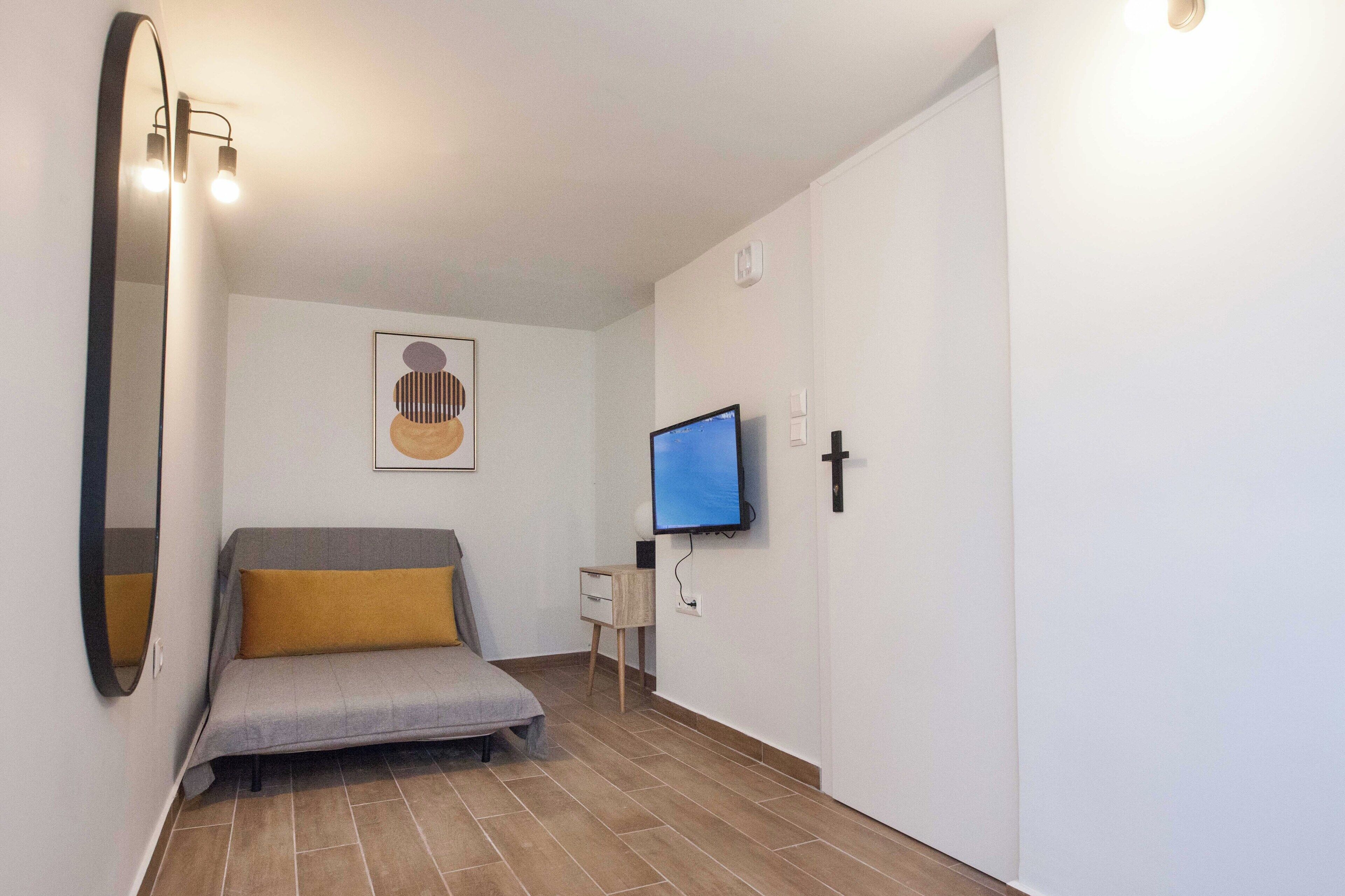A small, modern room with a bed, a TV, and a mirror.
