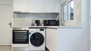 A compact kitchen with a built-in oven, a washing machine, and a coffee maker. - Cozy 1 Bd Basement Apt in Pagrati (Athens)